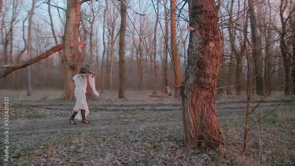 Cute young woman in image of witch and old Slavic costume runs through forest and performs movements corresponding to her image Cute young woman in image of witch and old Slavic costume runs through forest and performs movements corresponding to her image