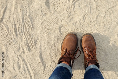 View from above to a pair of hiking trendy brown boots with shoelaces on sandy gritty background. Teenage and youth trendy casual shoes. Ready to journey! Travel activities concept. Hiking adventure.