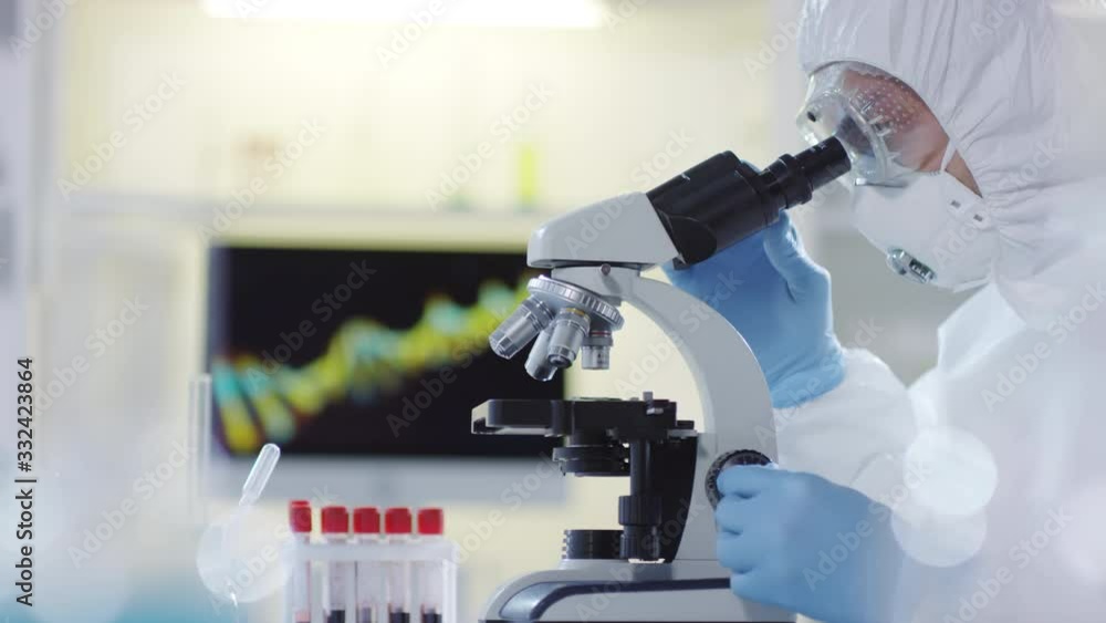 Side view shot of unrecognizable research scientist in hazmat suit, goggles and gloves looking at blood sample under microscope in laboratory