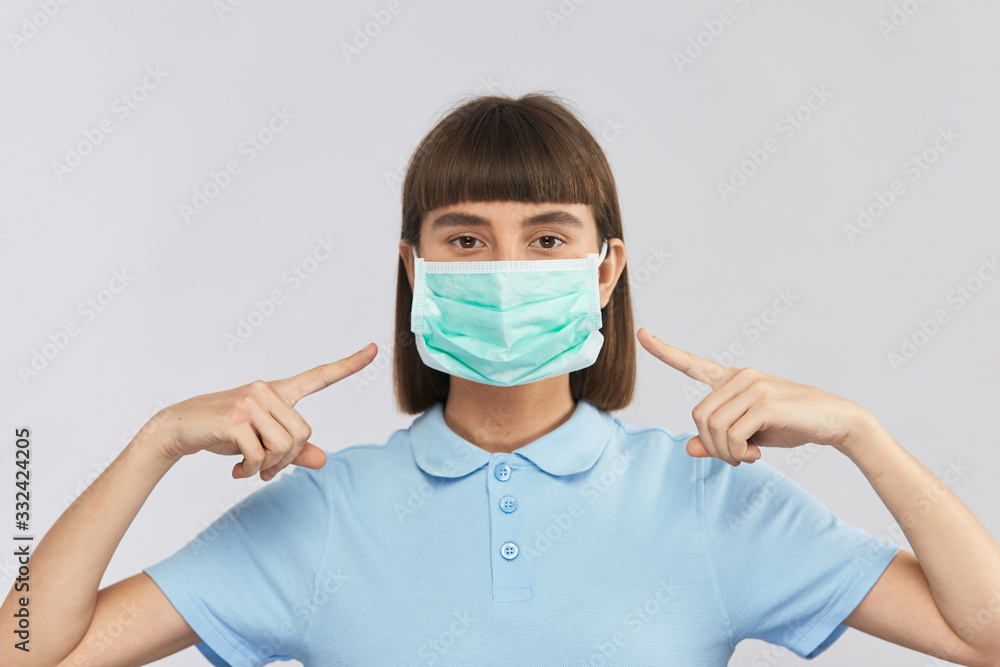 young serious girl wearing protection sterile mask and poiting with fingers on it young serious girl wearing protection sterile mask and poiting with fingers on it