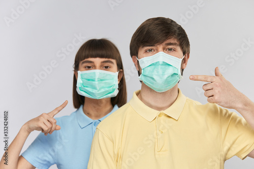 pretty people in protective mask pointing on it wearing yellow and blue shirts isolated on blue