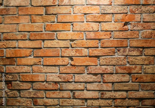 Brick wallpaper in a cafe is lit by a lamp from above. The wall of the old red brick in a bar 