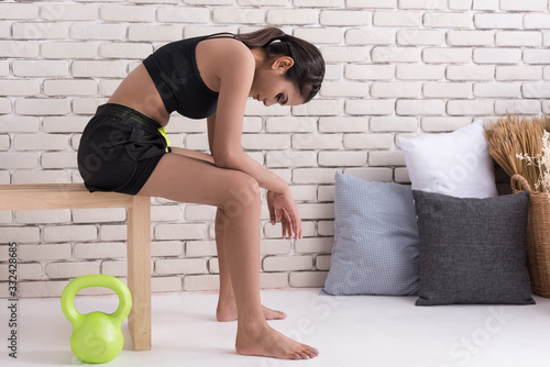 Woman sit on wooden chair in room, her head bow down, look tired after exercise. photo