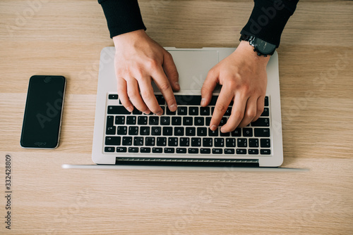 Man's hands using laptop with blank screen on desk in home interior. Mockup image white screen.