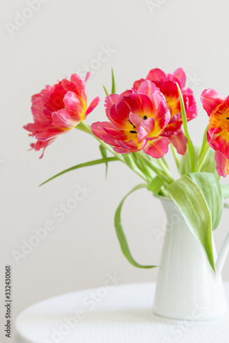 Red tulips bouquet in white vase on light background. Holiday background, close up. Valentine Day, Mothers day, birthday concept. Side view