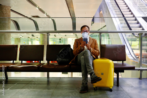 Man in mask at empty airport with luggage in coronavirus quarantine isolation, waiting for departure, flight cancellation, pandemic infection worldwide spread, travel restrictions and border shutdown photo