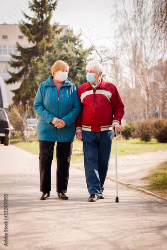 An elderly couple in protective masks walk along the street © Mallivan