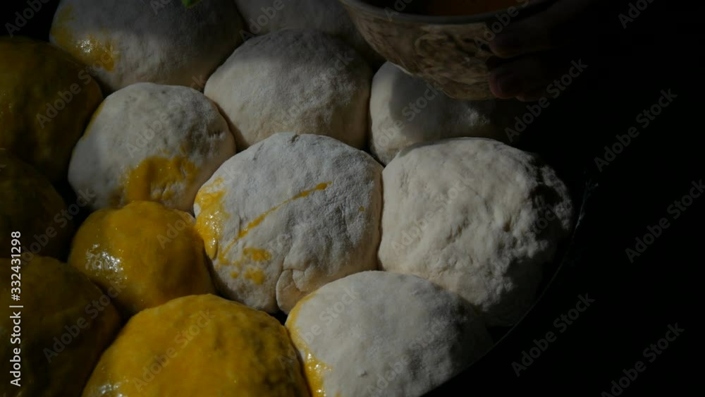 Homemade baking on a baking sheet, a female baker greases the balls from the dough with egg yolk. Special kitchen silicone brush for greasing dough. Ukrainian domestic dumplings. Homemade baking on a baking sheet, a female baker greases the balls from the dough with egg yolk. Special kitchen silicone brush for greasing dough. Ukrainian domestic dumplings.