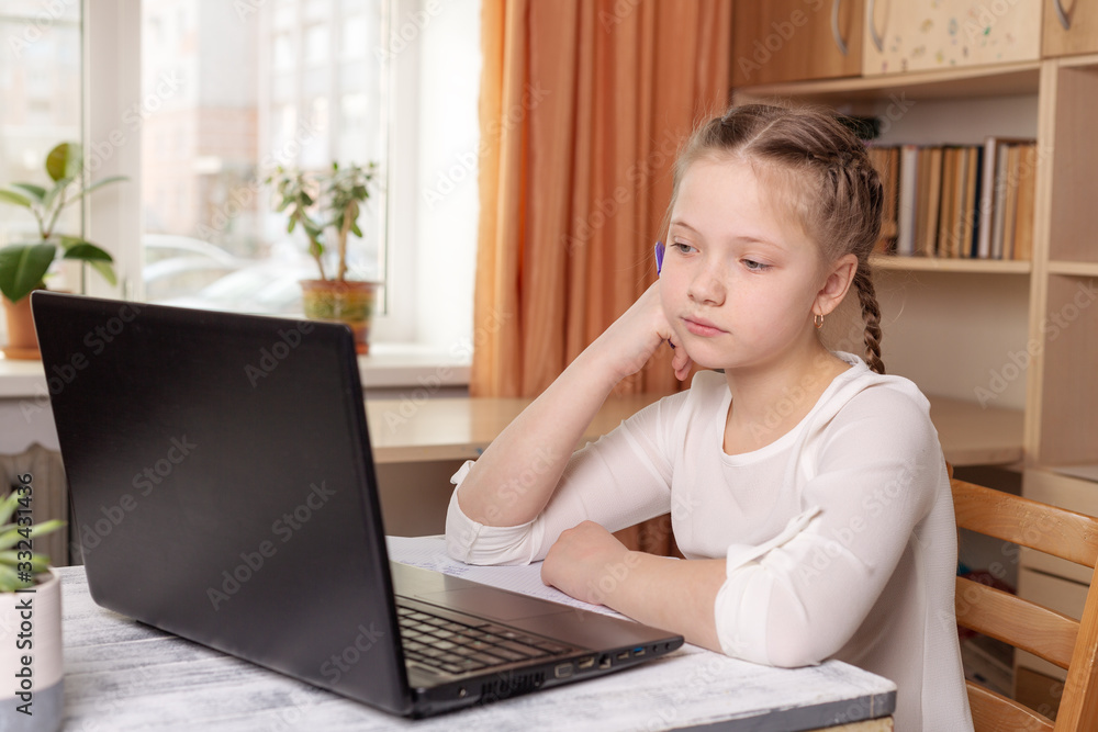 Serious schoolgirl looks at a laptop screen. Distance learning online education, home school, home education, quarantine concept Serious schoolgirl looks at a laptop screen. Distance learning online education, home school, home education, quarantine concept