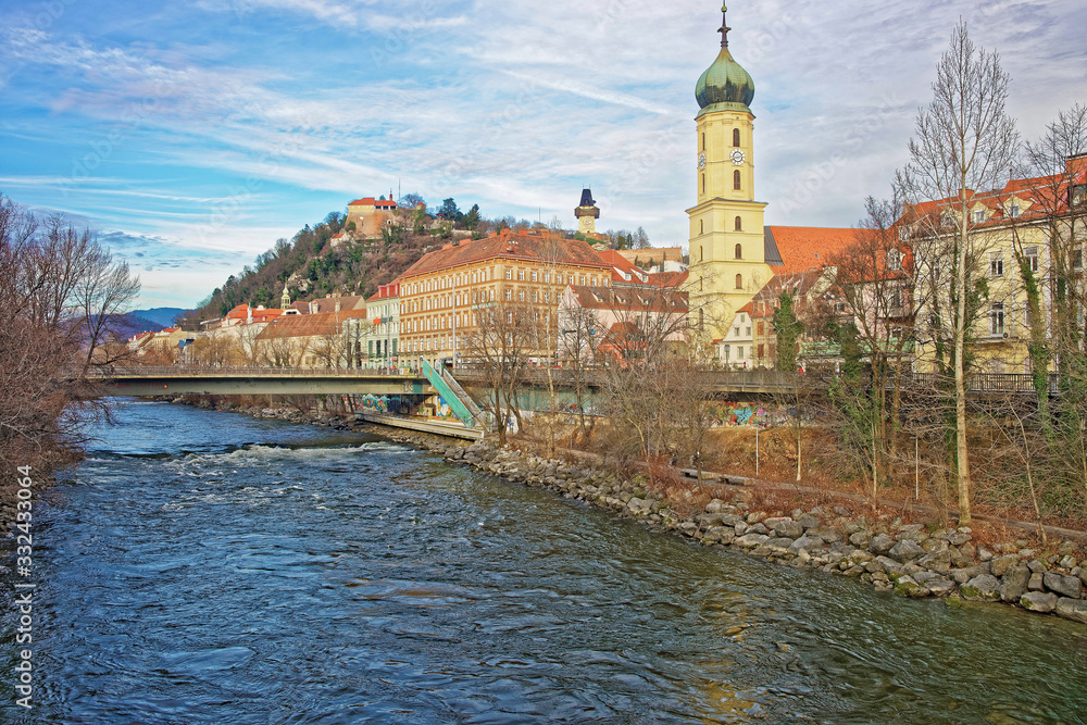 Obraz premium River view to the Franciscan church and Clock tower of the Castle Hill in Graz of Austria in January