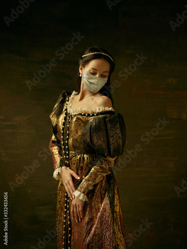 Medieval young woman as a duchess wearing protective mask against coronavirus spread on dark blue background. Concept of comparison of eras, healthcare, medicine and prevention against pandemic.