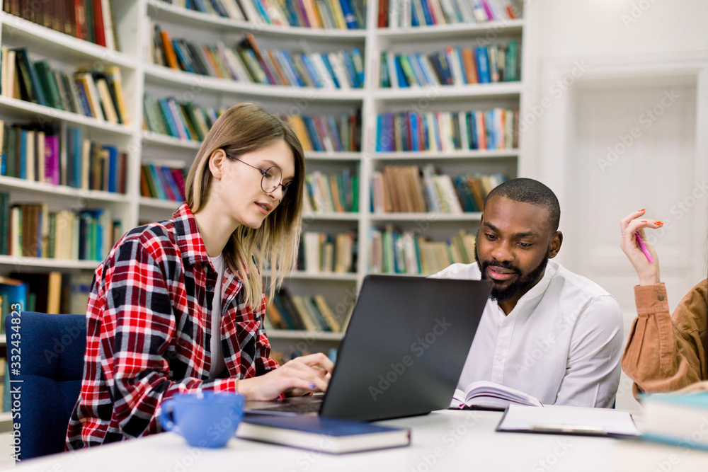 Group of college students studying in the university or school library, Caucasian girl and African boy are using a laptop and connecting to internet Group of college students studying in the university or school library, Caucasian girl and African boy are using a laptop and connecting to internet