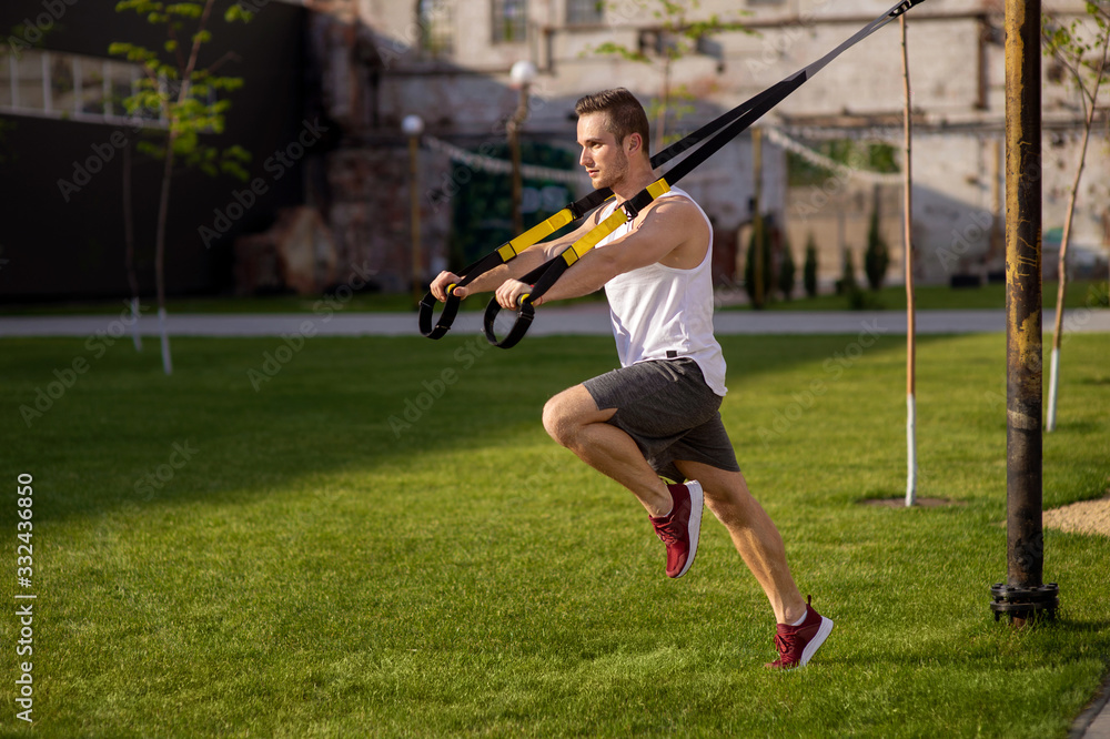 One man doing suspension straps exercises open air. Home workout routine. One man doing suspension straps exercises open air. Home workout routine.