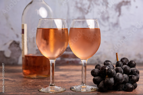 Wallpaper Mural Two wine glasses full of pink/red wine with grapes laying next to it and a bottle of wine in the background on the wooden table with a broken concrete background Torontodigital.ca