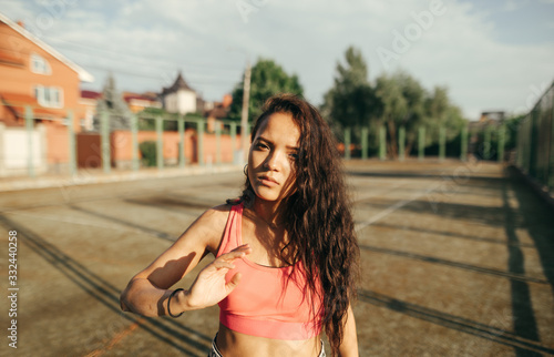 Closeup portrait of a Hispanic girl in sportswear standing on the playground at sunset, looking into the camera with a serious face.Fashionable girl in sportswear stands on old sport playground