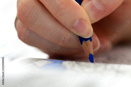 A close up portrait of a hand holding a blue colored pencil, whilst coloring in a book full of illustrations. A perfect way to relax from a hard day of work is with your hobby.