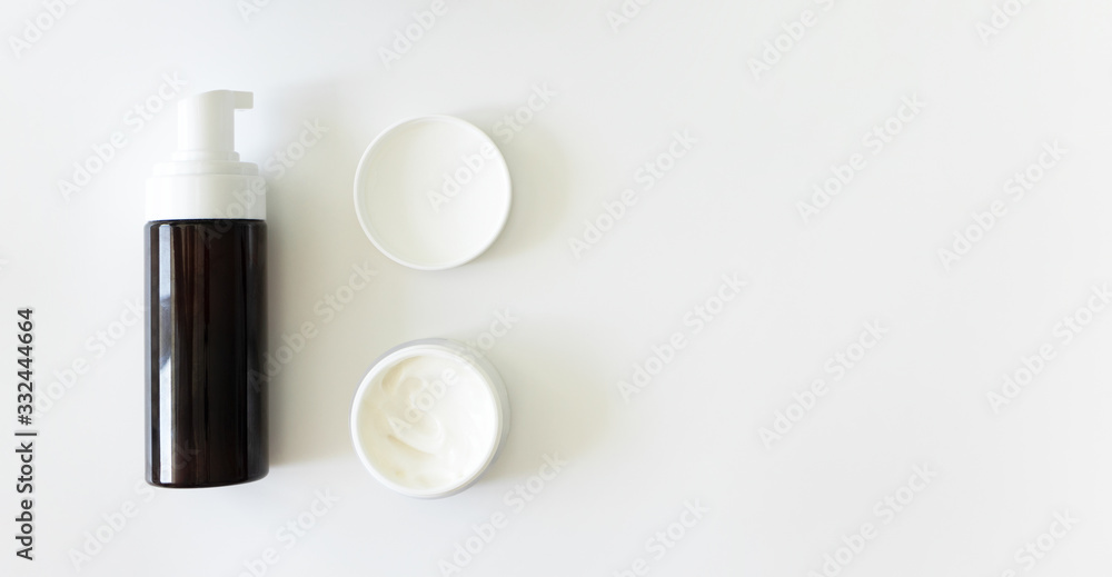 Cleanser foam in brown container with dispenser and moisturizer cream mockup bottles on white background with copy space, banner format. Step facial skincare, top view. Cleanser foam in brown container with dispenser and moisturizer cream mockup bottles on white background with copy space, banner format. Step facial skincare, top view.