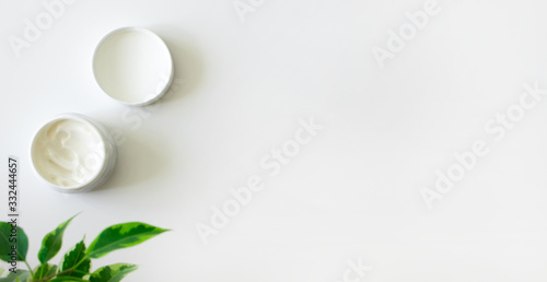 Face moisturizer cream and fresh green leaves on white background witn copy space, banner format. Concept natural bio organic cosmetic