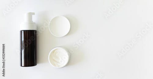 Cleanser foam in brown container with dispenser and moisturizer cream mockup bottles on white background with copy space, banner format. Step facial skincare, top view.