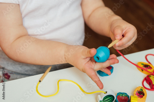 Child putting beads on a string. Bead stringing activity. Fine motor skills development. Lacing, threading.
