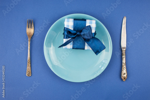 ceramic plate with a cutlery and gift box on the blue paper background