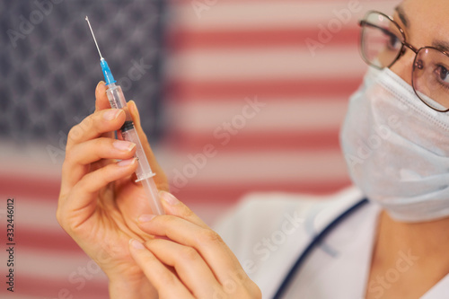 doctor is standing against the background of the US flag in the hands of a syringe in the vaccine. Novel coronavirus 2019-nCoV