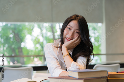 Beautiful student wearing white shirt resting while reading books on the table in library