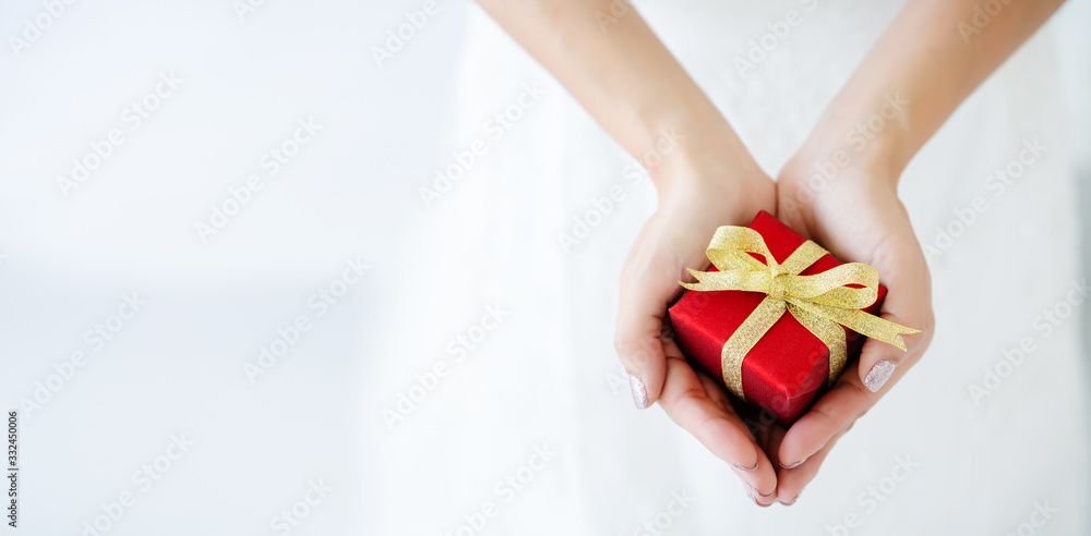 Red gift box with a golden bow tied on a woman's hand. Business Online delivery concepts Red gift box with a golden bow tied on a woman's hand. Business Online delivery concepts