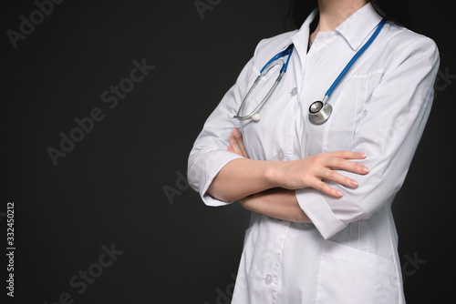 Doctor with stethoscope is standing with crossed arms close up on dark background with copy space.