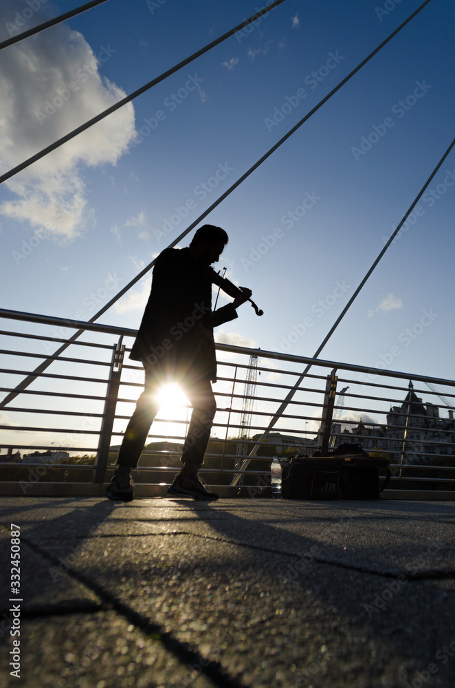 Silhouette of a man playing the violin on a bright afternoon as the sun seeps under his legs