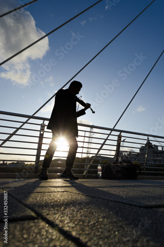 Silhouette of a man playing the violin on a bright afternoon as the sun seeps under his legs