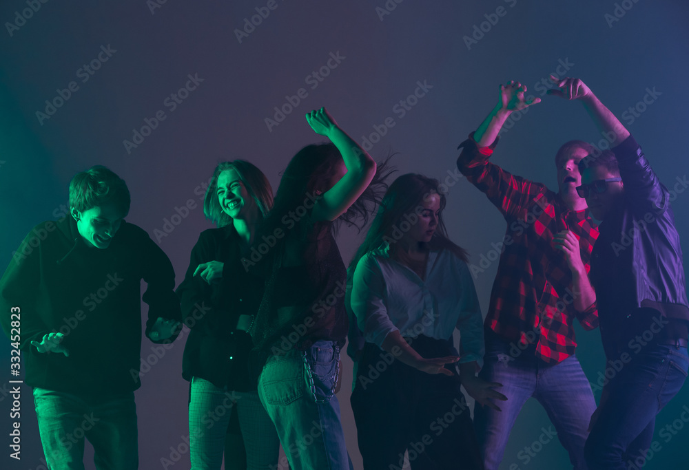 Fototapeta premium Cheering dance party, performance concept. Crowd shadow of people dancing with neon colorful lights raised hands up on dark background. Celebration, holiday, weekend, nightlife and positive vibes.