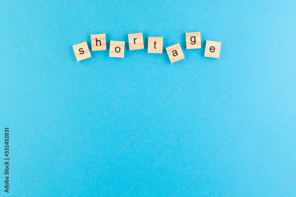 Obraz premium The inscription Shortage laid out of wooden cubes on a blue background.