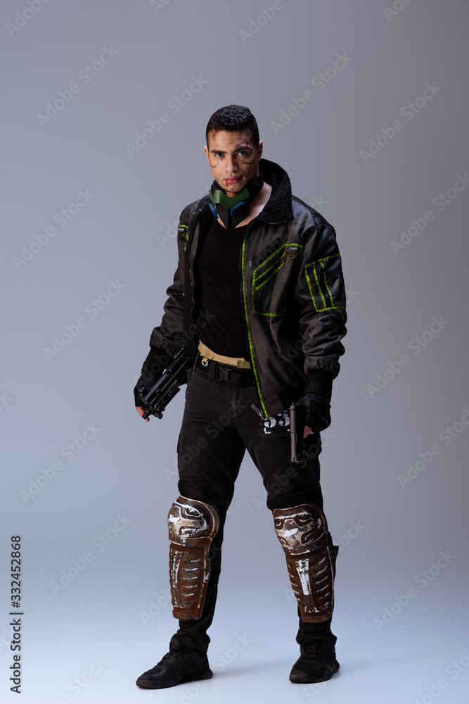 mixed race cyberpunk player with mask holding gun while standing on grey mixed race cyberpunk player with mask holding gun while standing on grey