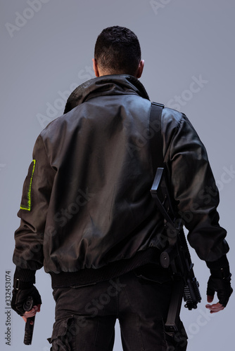 back view of cyberpunk player holding gun while standing on grey