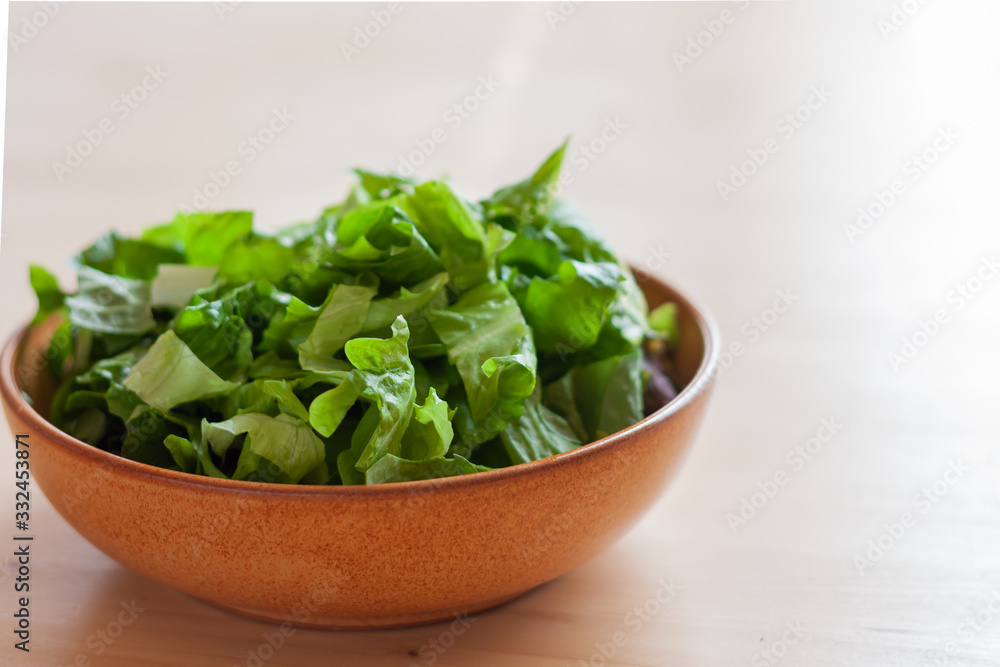 green salad of lattuce in natural ceramic plate on wooden light background. Space for text. green salad of lattuce in natural ceramic plate on wooden light background. Space for text.