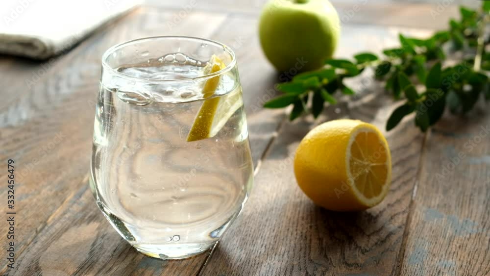 Slow motion of lemon slice falling into glass of water. Fresh clean water with lemon in glass. Weight loss, healthy lifestyle concept Slow motion of lemon slice falling into glass of water. Fresh clean water with lemon in glass. Weight loss, healthy lifestyle concept