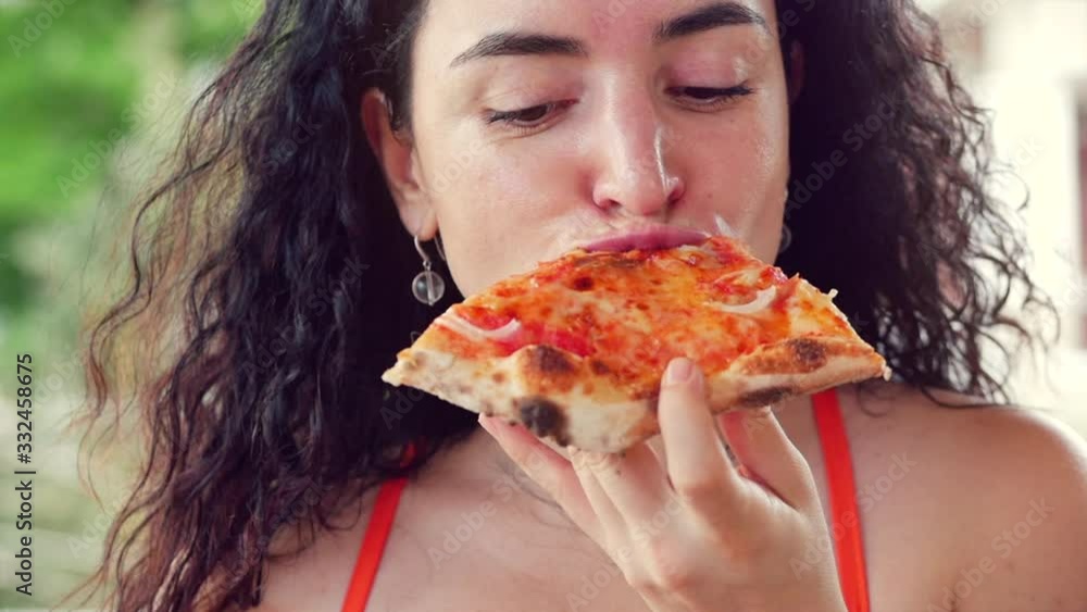 Young cute Italian-looking woman in a red dress eagerly eating and enjoying Italian pizza while in a restaurant. The concept of female food, nutrition, calories. Young cute Italian-looking woman in a red dress eagerly eating and enjoying Italian pizza while in a restaurant. The concept of female food, nutrition, calories.