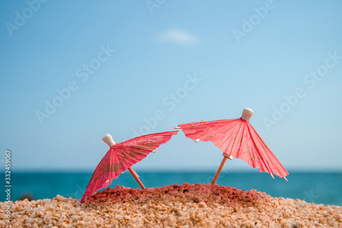 Photography Tiny red umbrellas by the sea in the sand