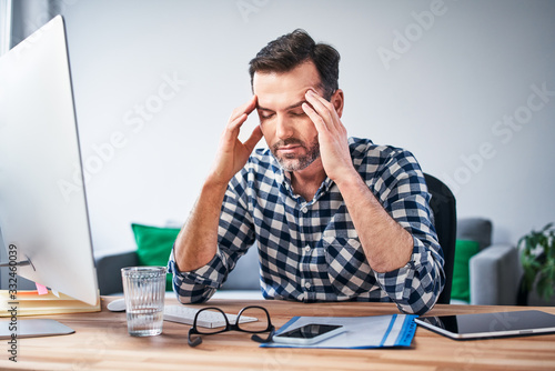 Overworked man suffering migraine, working on computer from home office