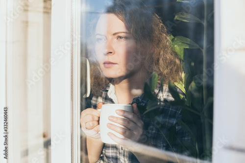 Foto Young blonde woman looking out of the window with a concerned expression on her