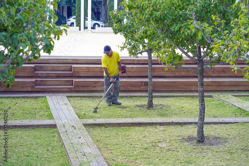 Man cutting grass in a park. Elderly man worker mowing lawn with grass trimmer outdoors on sunny day.