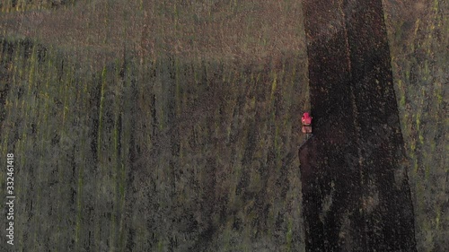 Top view tracking shot of red tractor with plow riding and plowing soil agricultural field in countryside