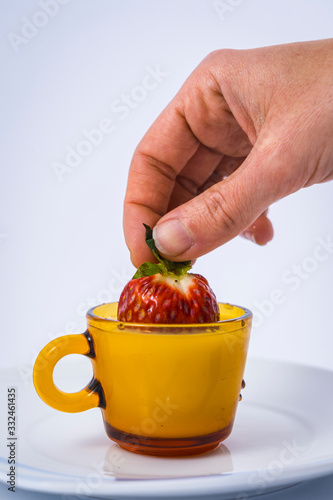 A wet strawberry in a milk cup held by a woman's hand with white background