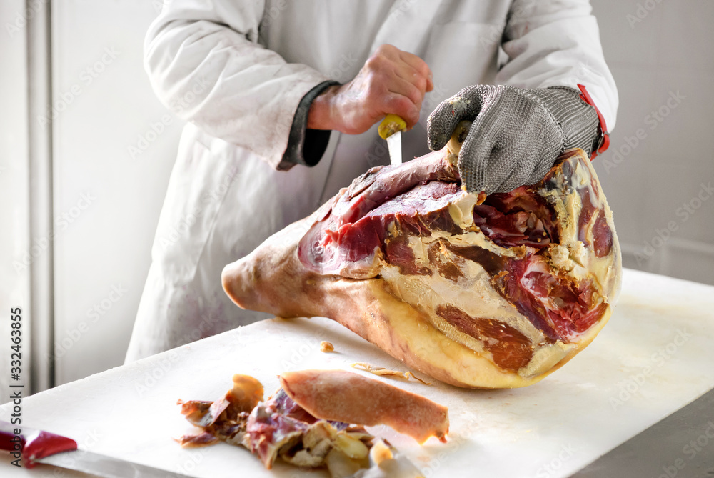 Butcher works on ham, using metal glove