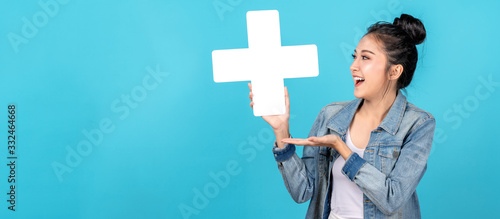 Banner of asian woman smiling, showing plus or add sign and other hand open on blue background. Cute asia girl wearing casual jeans shirt and showing join sign for increse and more benefit concept