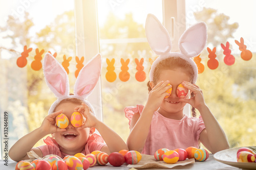Photography Cute girls holding yellow easter eggs instead of eyes and laughs, having fun on a background of windows