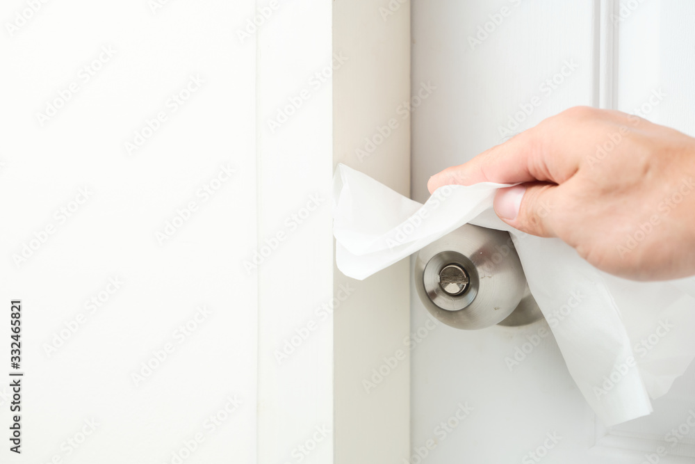 Obraz premium Hand cleaning the doorknobs with white facial tissue of the closed white door closed. Health concept to aware for touching the everyday objects.