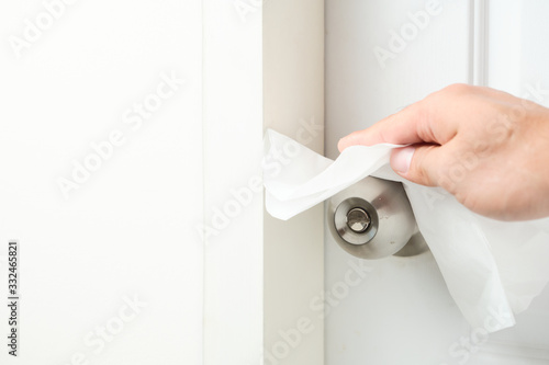 Hand cleaning the doorknobs with white facial tissue of the closed white door closed. Health concept to aware for touching the everyday objects.