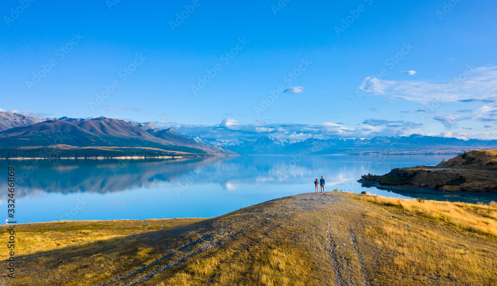 Viewpoint at sunrise where two young people enjoying the beautiful view of the calm lake and snowy  mountains in the back